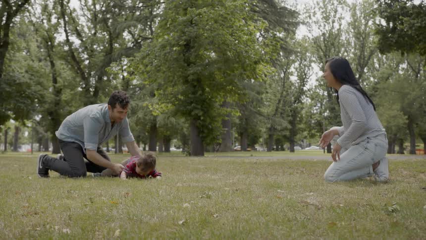 A man and woman play with their baby in a park