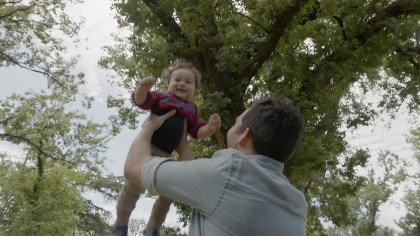 Father playing with son on a park next to a tree