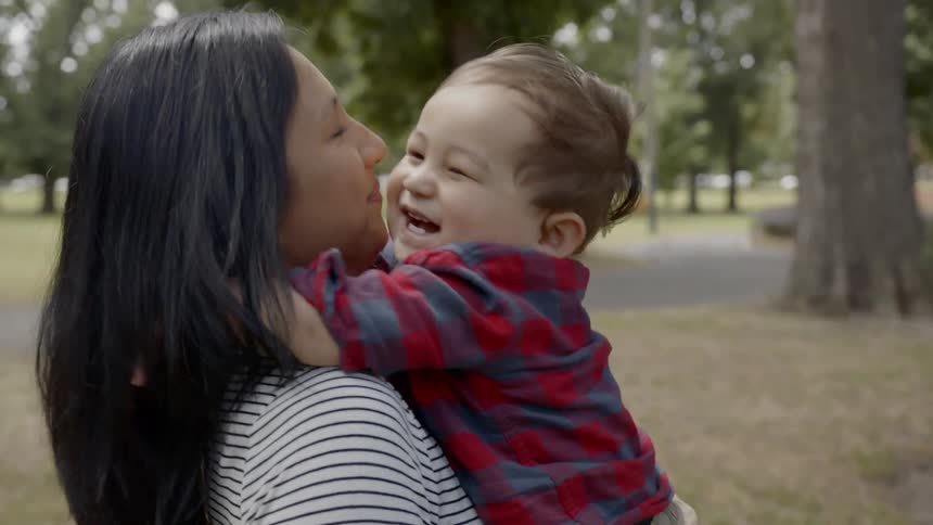 A hispanic woman smiles and hugs her laughing son