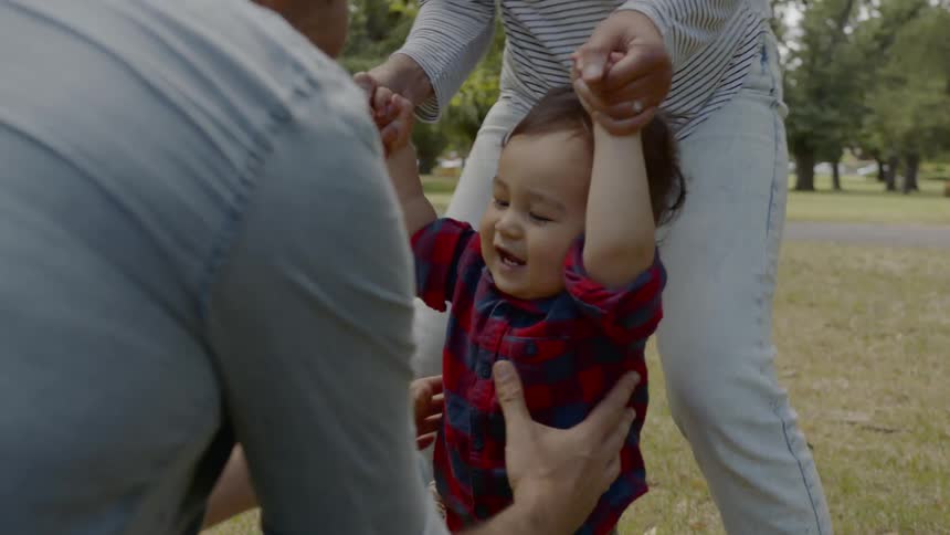 A woman helps a little boy walk to a man