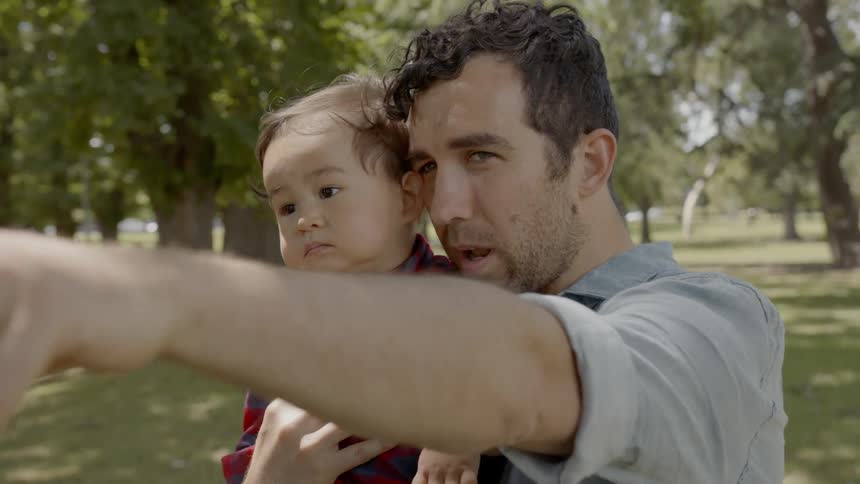 A man and young son point at something while standing in a park