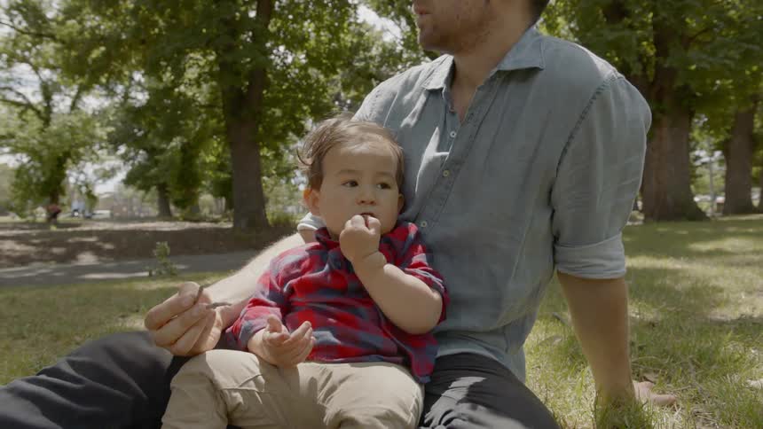 A man sitting on the grass with a baby sitting on his lap