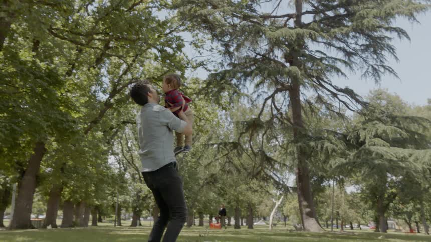 A man in a park picking up a baby with a woman and a dog in the background