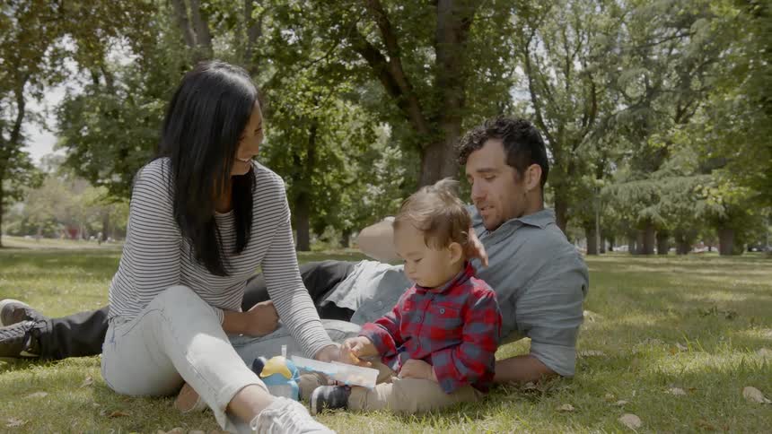 A family are sitting together in the grass of the park talking