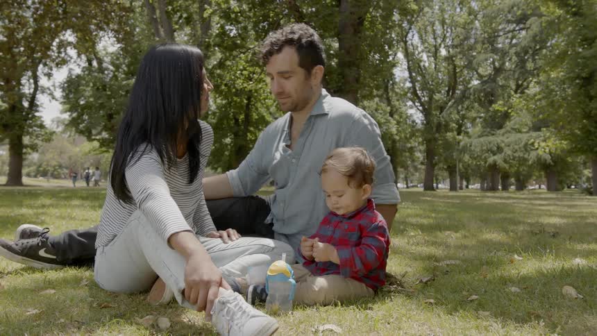 Family sit on outdoors on grass on sunny day