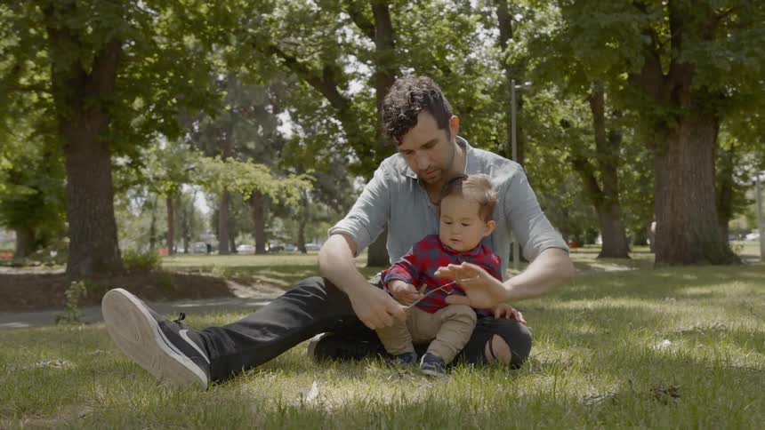 A man is sitting in the grass playing with his son in the park