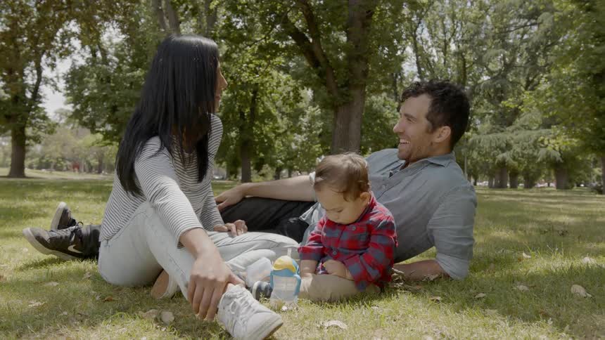 Husband wife and child are sitting outside in the grass