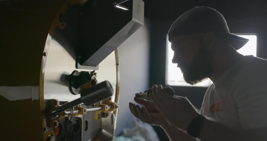 A man taking coffee beans out of a machine and smelling it