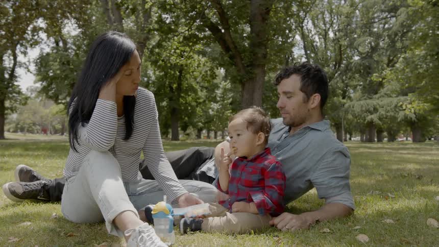 A husband wife and child sitting on the grass in the park