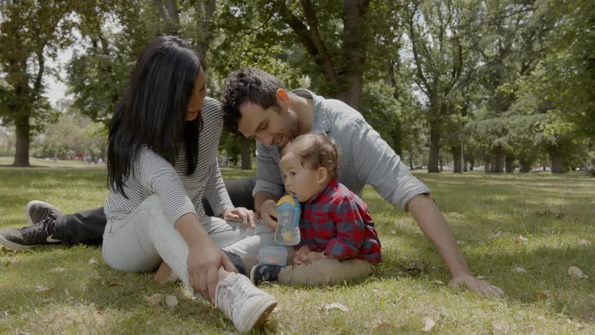 Family sits on grass in park as toddler eats