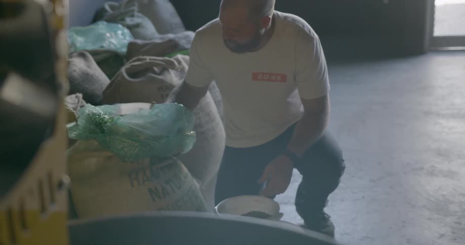 Man crouch on concrete floor scooping coffee beans from sack into bucket