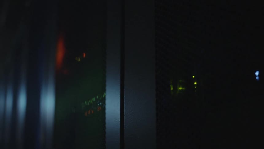 Server racks have several pieces of equipment in them with flashing led lights in a dark room
