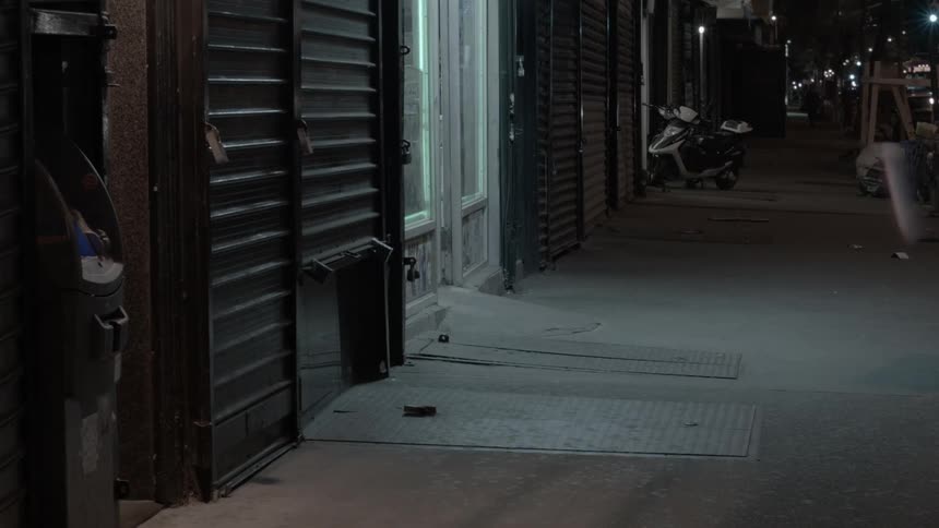 A storefront at nighttime with people and vehicles in the background