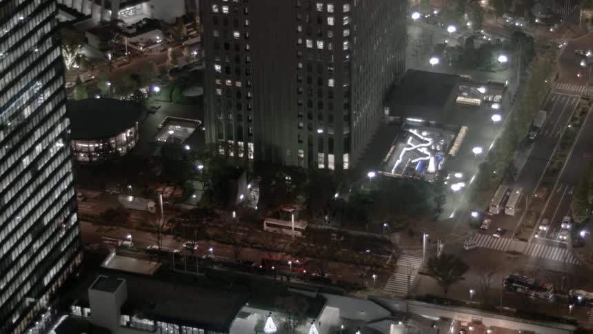 Traffic moves through intersection near lit skyscrapers at night