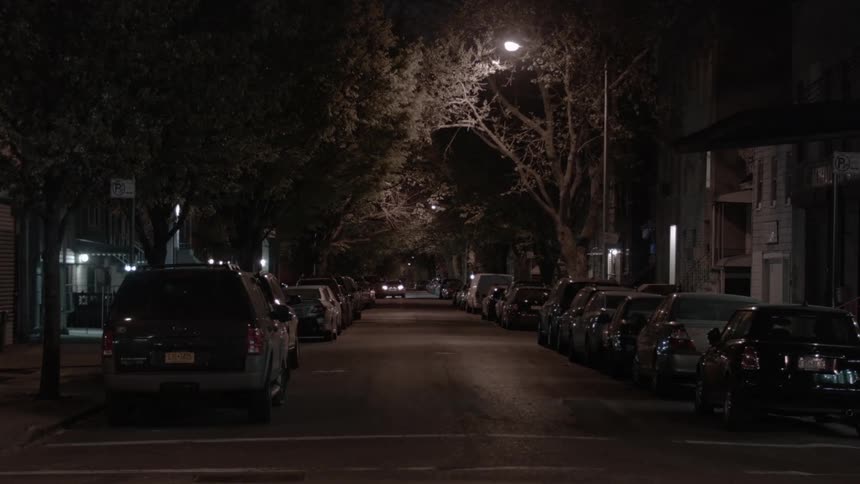 A neighborhood street at night with a car double park with hazard lights flashing
