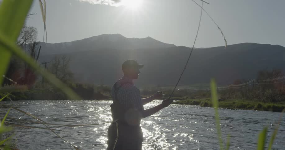 A man stands in a lake and throws a fishing line out