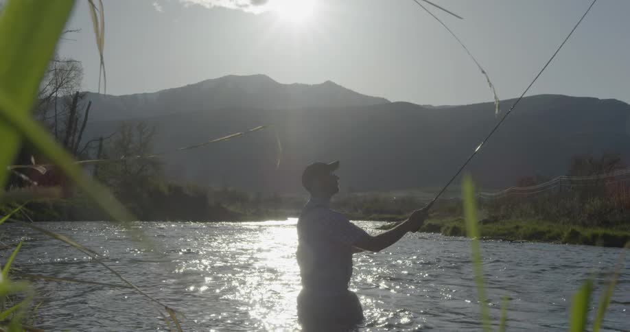 A man wades in a river while fishing on a sunny day