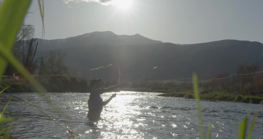 A man stands in the lake to cast a fishing pole
