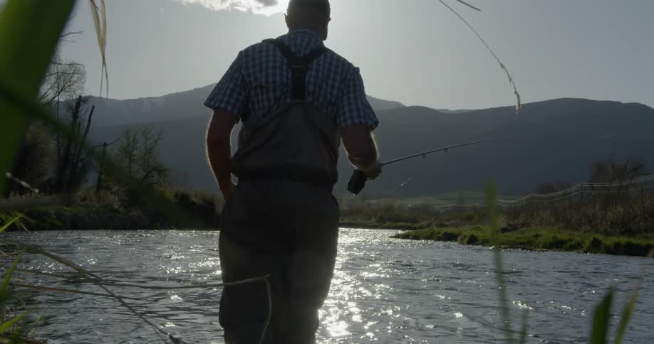 Man wades into river holding fishing rod and reel