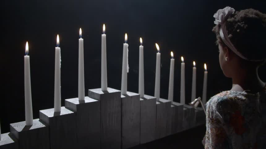 A girl walking past a row of lit candles on wooden blocks