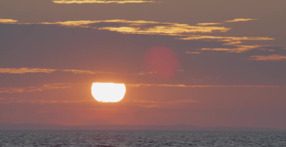 The sun shines through clouds at sunset over an ocean