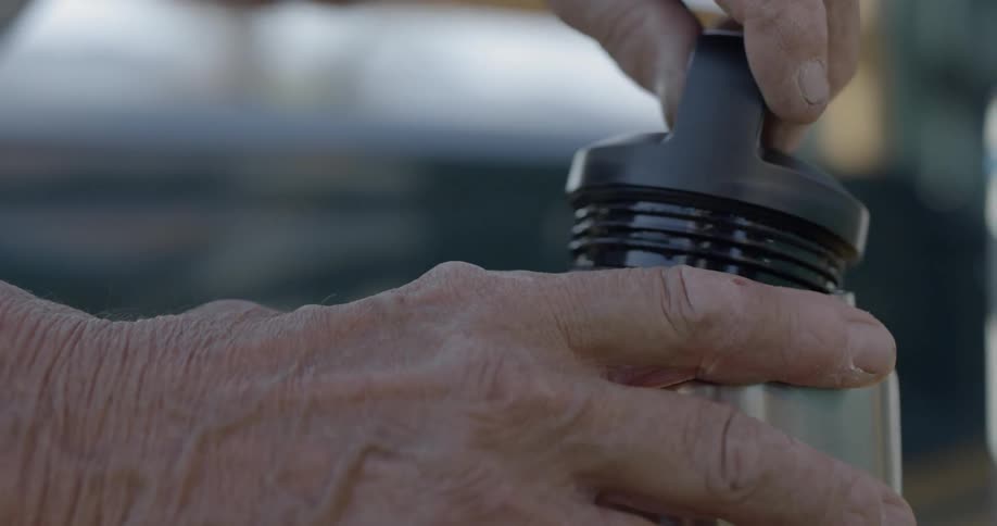 A man twists the cap off of a thermos and steams pours out the top