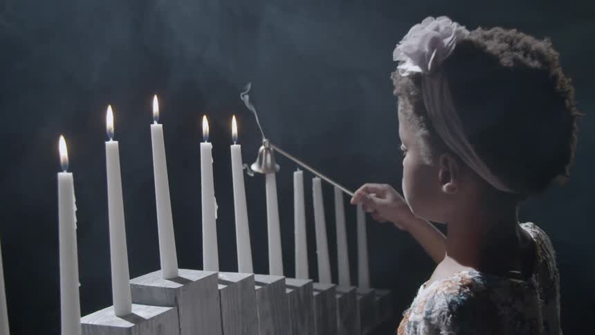 A black girl puts out a long candle with a candle snuffer