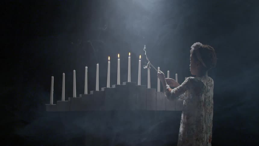 A girl outing a white candle on a concrete pedestal