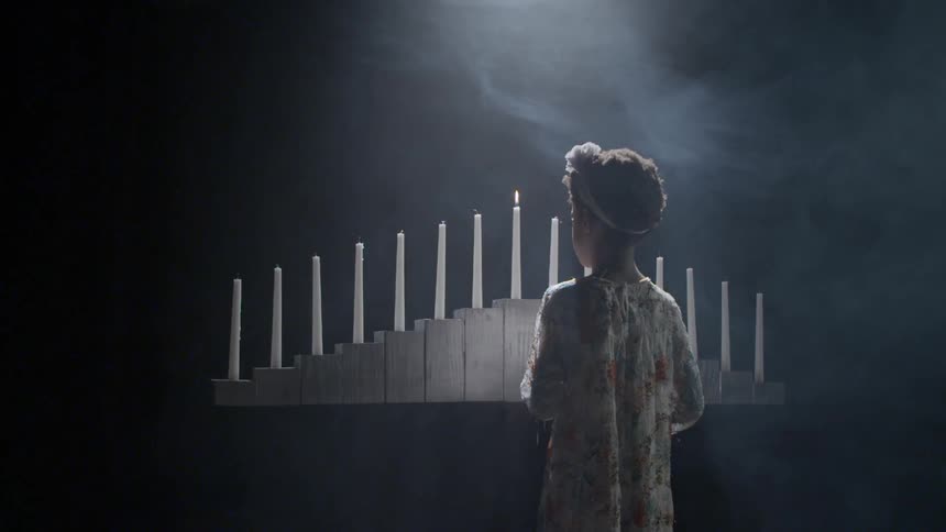 A young black girl stands and watches a burning candle