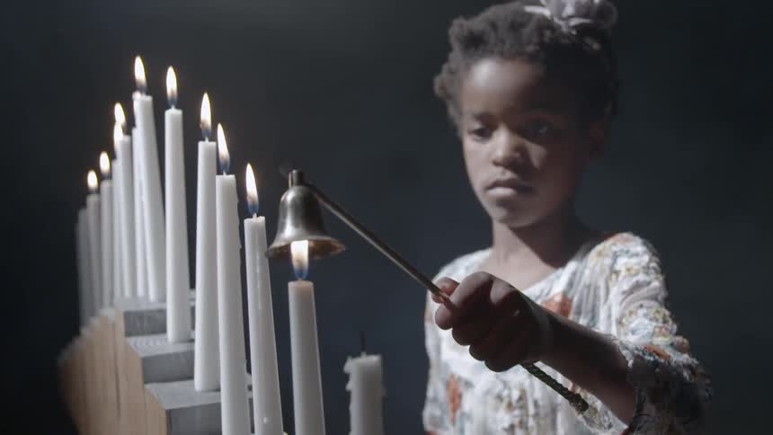 A young black girl puts out a candle flame with a candle snuffer