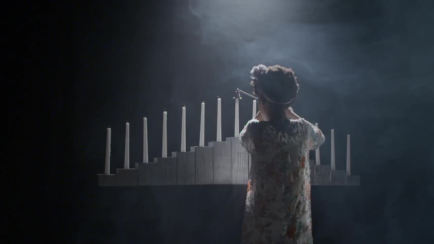 A young girl raises a candle snuffer to put out the last candle and it smokes after the flame is out