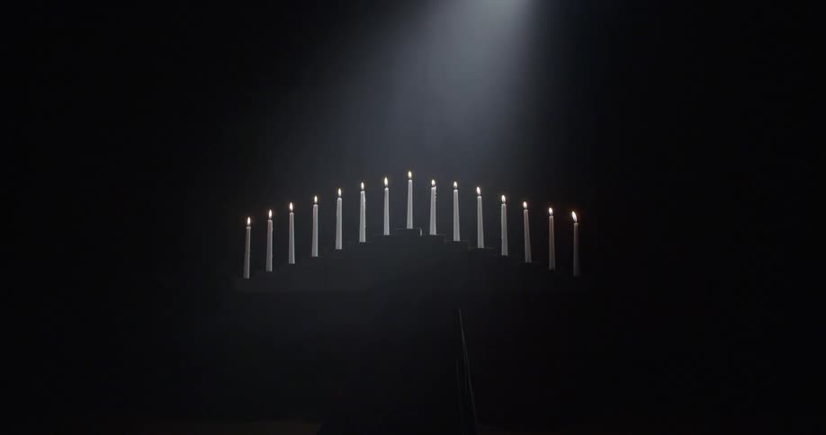 Several white candles are lit in a dark room