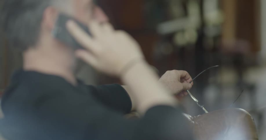 A man holds his glasses while talking on a cell phone