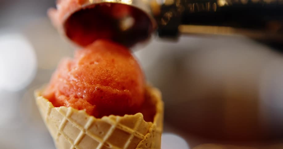 A person scoops orange sherbet into a waffle cone