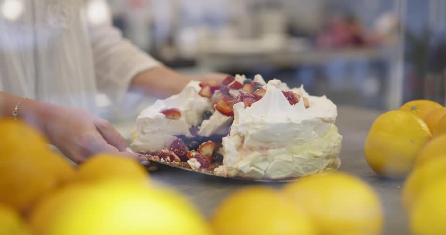 A baker brings out a fruit topped cake with a large piece missing