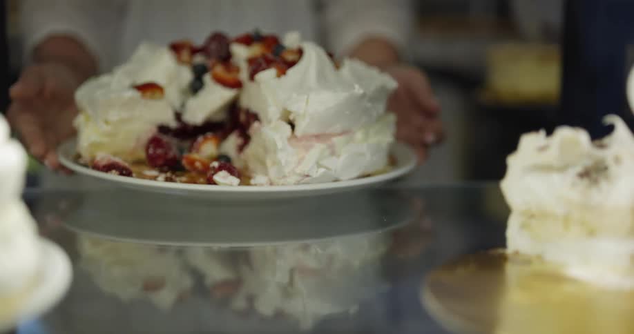 A person picks up a cake with whipped cream and fruit on it