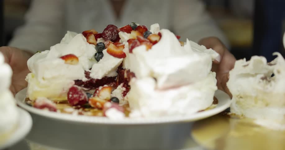 A person in white placing a plate of cake with a slice missing on a table
