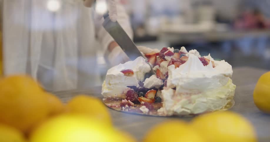 A woman puts a cake next to lemons on a wood table and cuts a slice