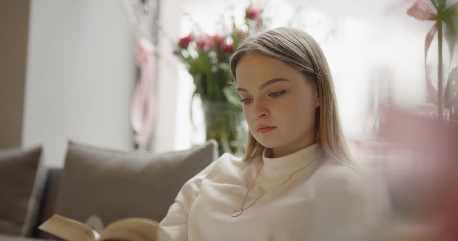 A woman is indoors and reading a book