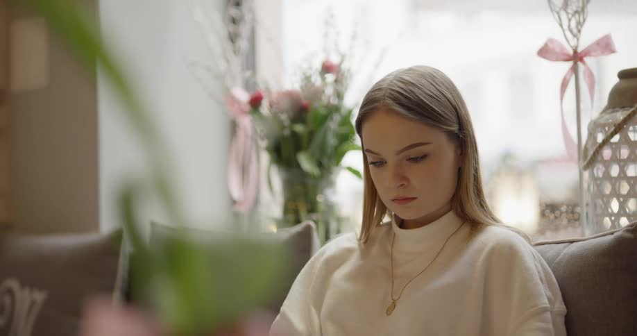 A blonde white woman sits on a couch looking at a book