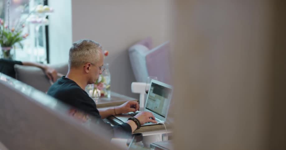 A man types on a laptop sitting in a public space