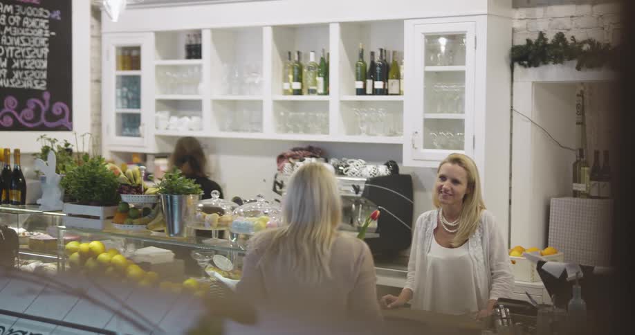 Two blonde women speak at a restaurant counter