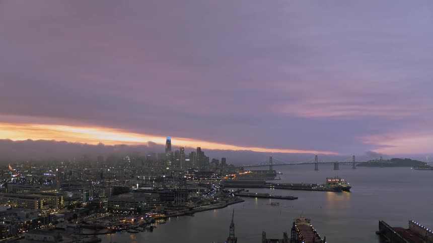 A metropolitan area near a bay lights up at sunset