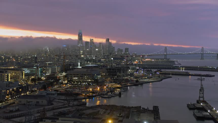 Skyline of the illuminated city with skyscrapers and tall buildings next to the sea at sunset