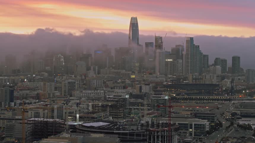 A skyscraper towers over the other buildings in a city skyline at sunset