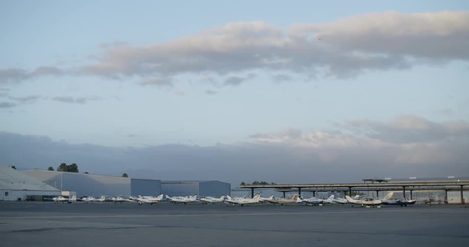 Small aircraft sit on the tarmac at an airport on a cloudy day