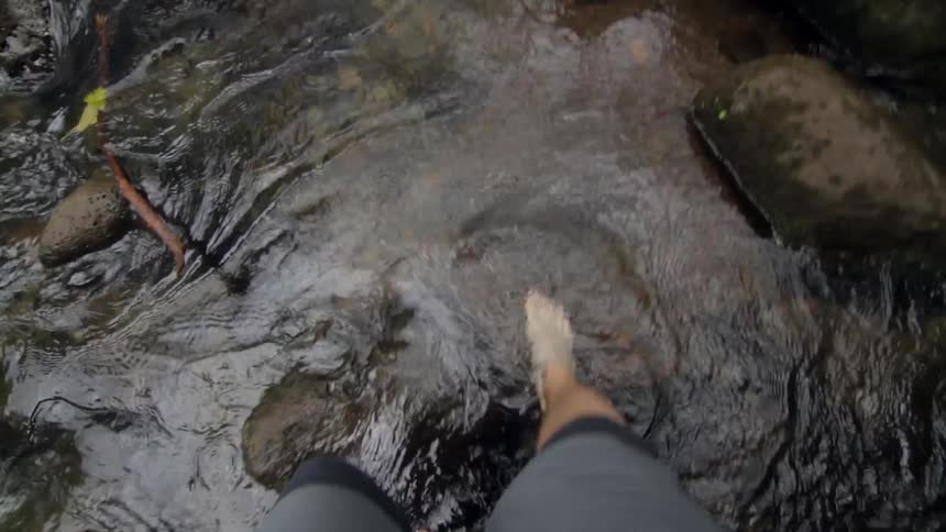 A man is walking in a body of water with rocks in it