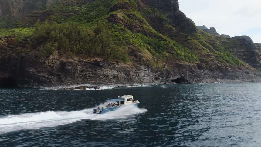 A tug boats moves quickly through the water next to large hills and mountains