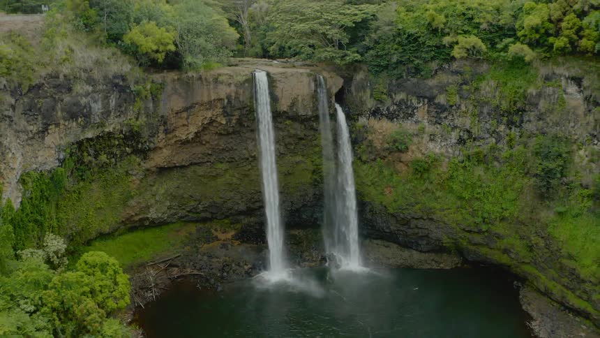 An aerial view of 2 waterfall that drop to a lake on the forest