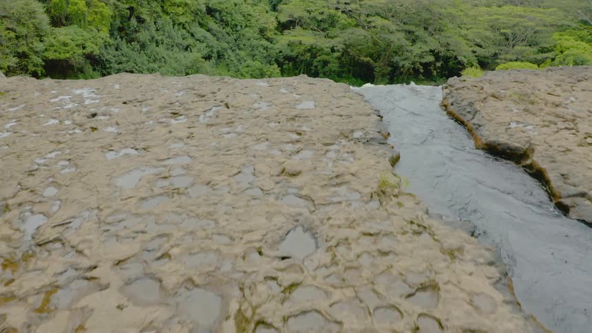 A stream flows over a cliff into a pool of water below in the wilderness